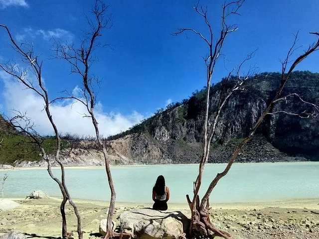 Una mujer se sienta en una roca frente al lago del cráter Kawah Putih.
