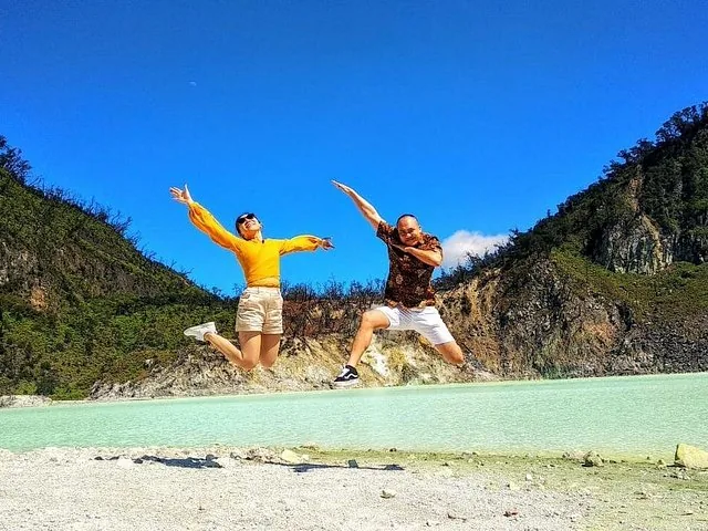 Two tourists jumping joyfully on the white shores of Kawah Putih crater lake.