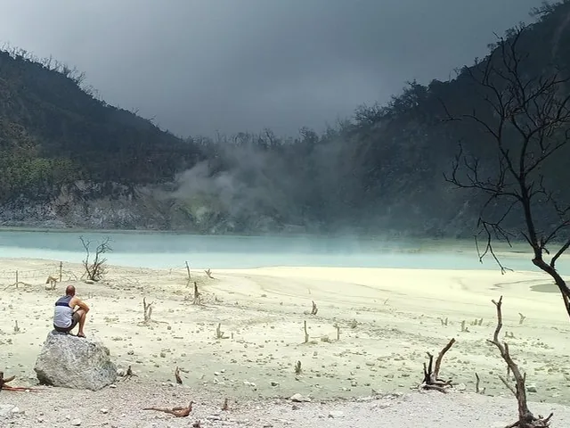 A person sitting on a rock by the pale blue water at Kawah Putih.