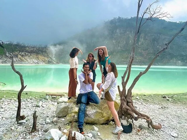 Eine Gruppe von Freunden posiert fröhlich am helltürkisfarbenen Wasser des Kawah Putih.