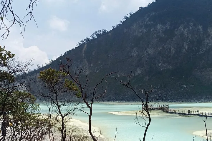 Un lago de cráter volcánico de color azul pálido con un muelle de madera y colinas alrededor.